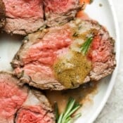 A plate with three slices of beef tenderloin on it, pan juices and a piece of rosemary.
