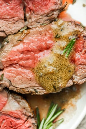 A plate with three slices of beef tenderloin on it, pan juices and a piece of rosemary.
