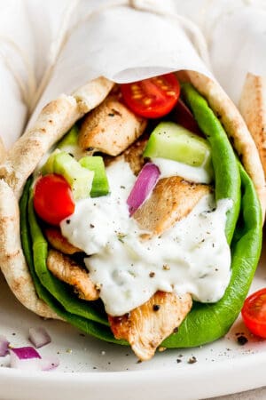 Close up shot of a chicken gyro with tomatoes, cucumbers and red onion.
