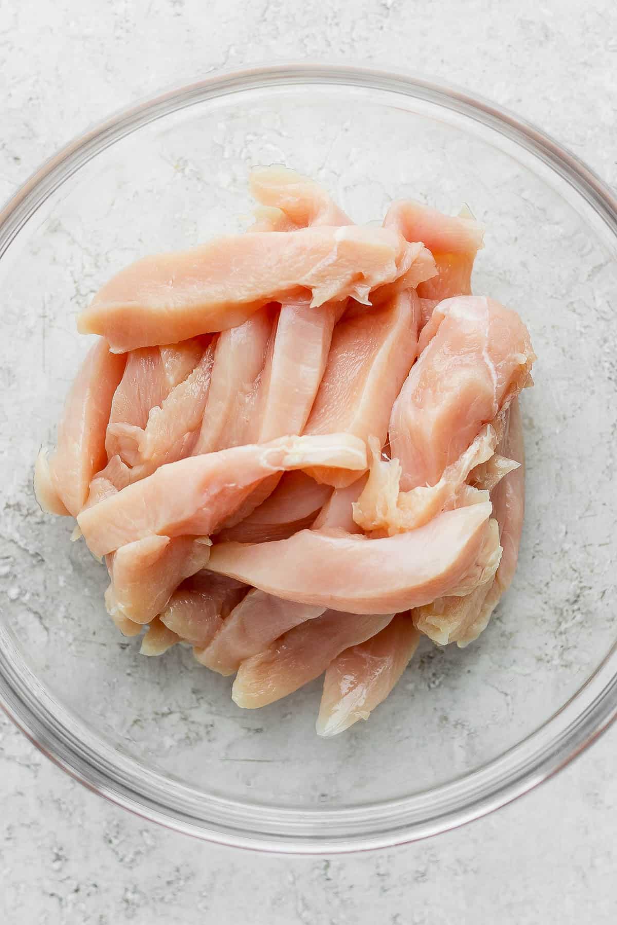 Raw chicken cut into tenders and placed in a glass bowl.