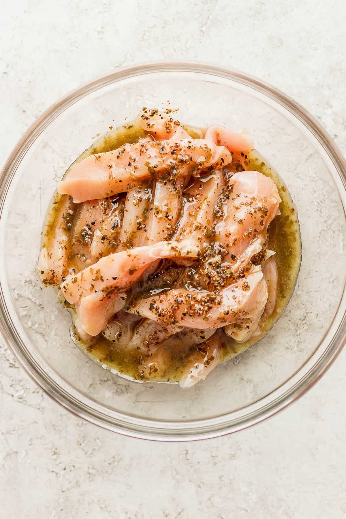 Chicken tenders in a glass bowl with the greek marinade on top.