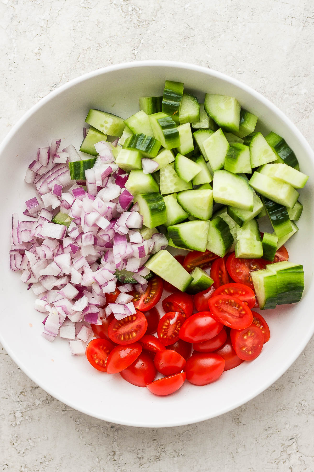 Fresh tomatoes, cucumbers, and red onion on a white plate.