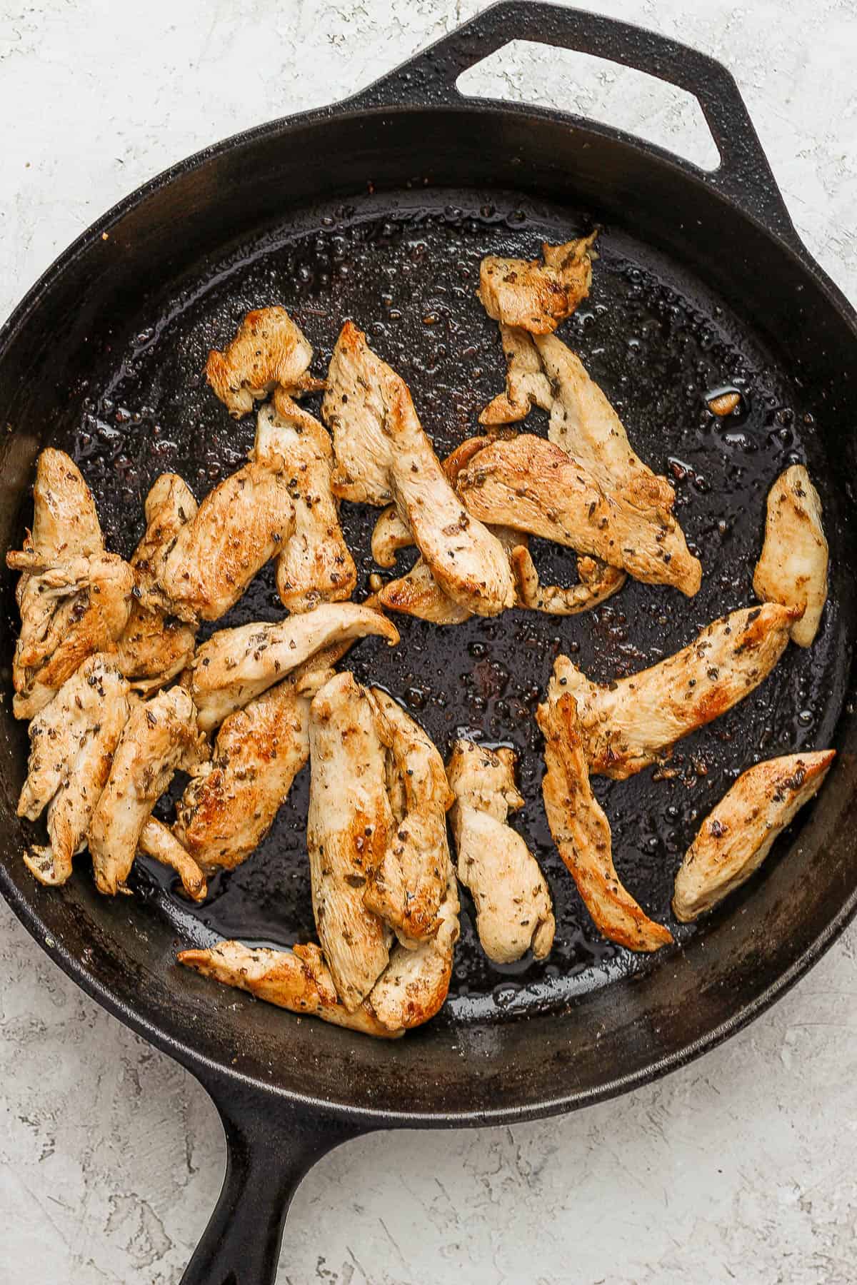 Marinated chicken tenders cooking in a large cast iron skillet.