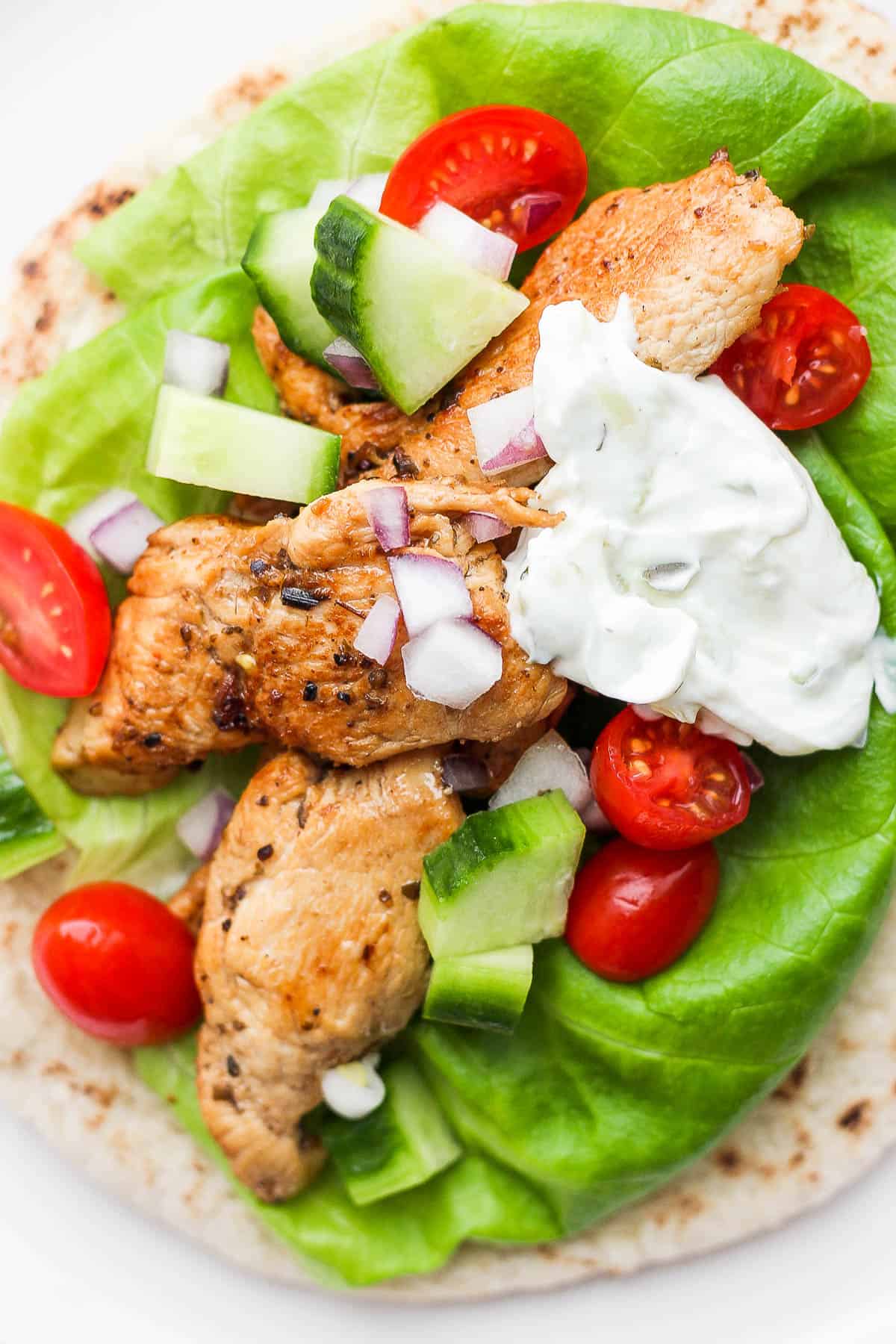 A pita bread with lettuce, chicken, veggies, and sauce on top.