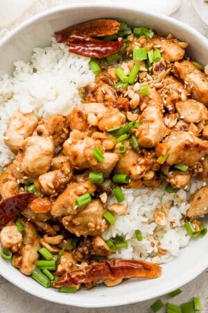 Bowl of kung pao chicken with rice and green onions on top.