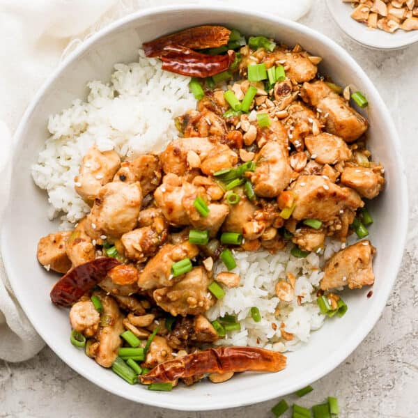 Bowl of kung pao chicken with rice and green onions on top.