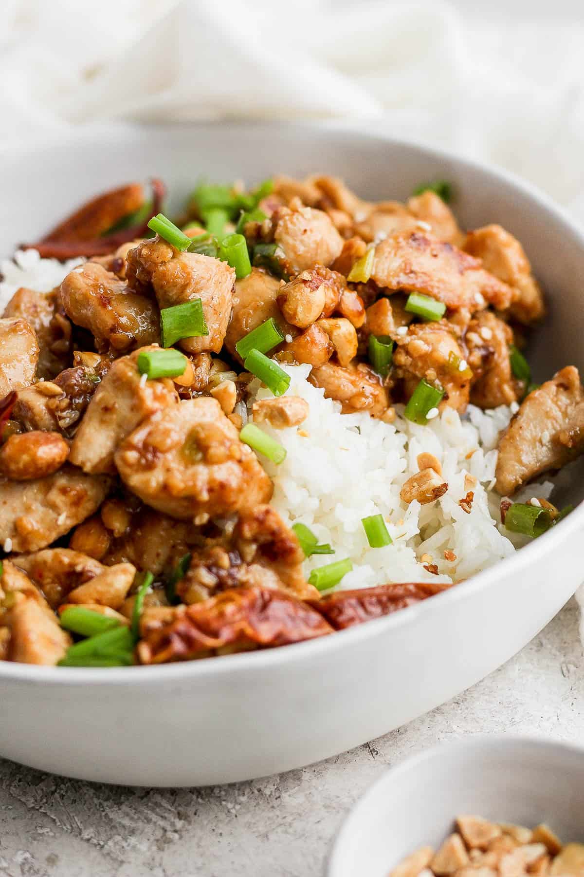 Kung pao chicken over rice in a white bowl.