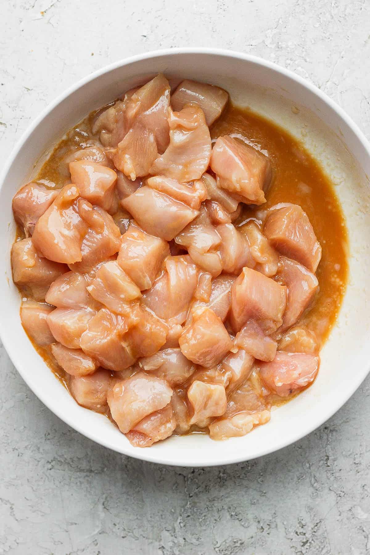 Chicken mixed with the marinade in a white bowl.