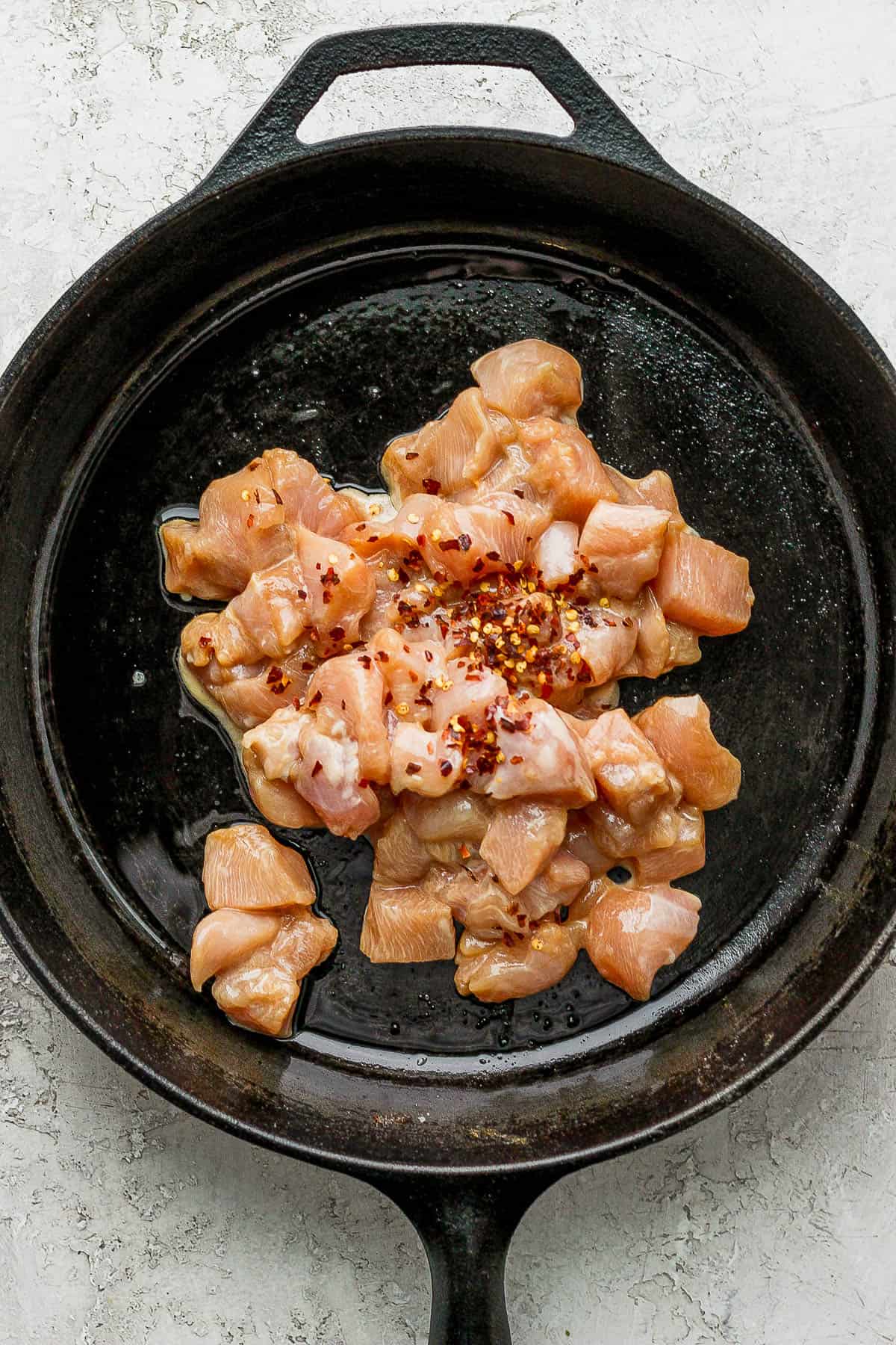 Marinated chicken added to a cast iron skillet with red pepper flakes.