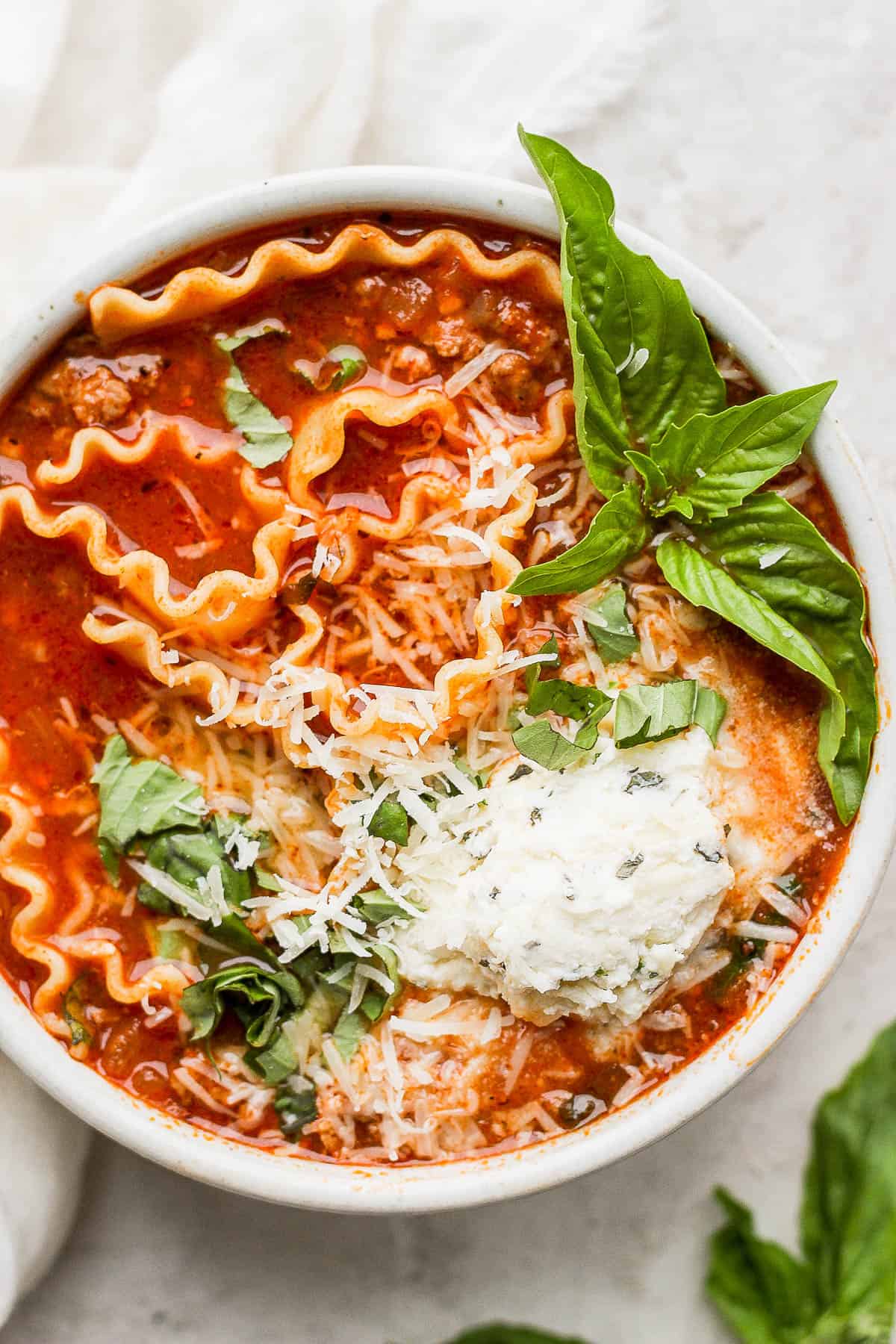 Lasagna soup in a bowl with the ricotta mixture, parmesan cheese, and fresh basil on top.