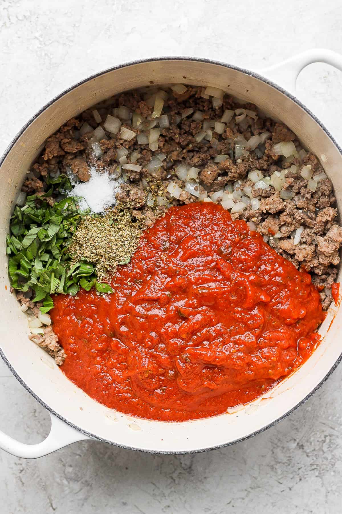 Marinara sauce, oregano, basil, salt, and pepper added to the pot.