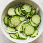 Bowl of marinated cucumbers with onion, garlic and sesame seeds on top.