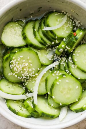 Bowl of marinated cucumbers with onion, garlic and sesame seeds on top.