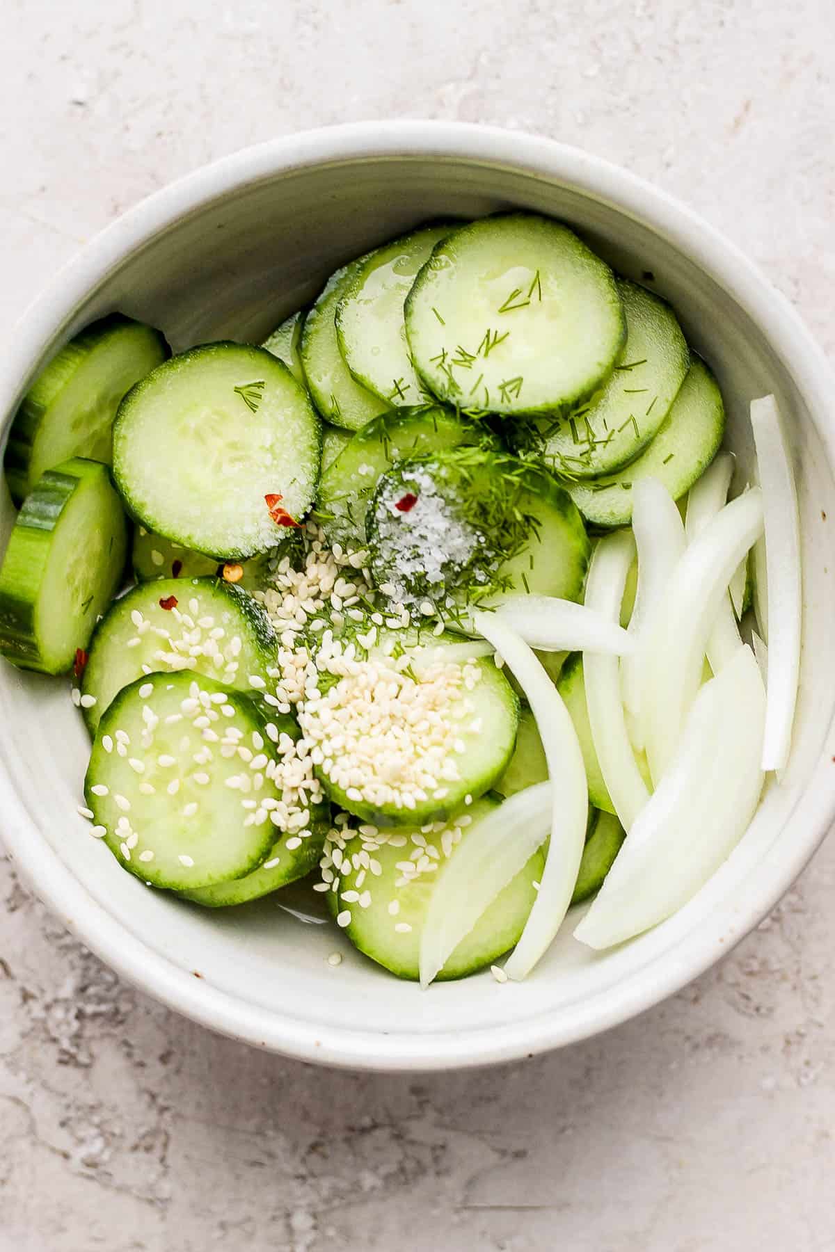 Cucumbers, onion, vinegars, salt, sesame seeds, and red pepper flakes all in the same bowl.