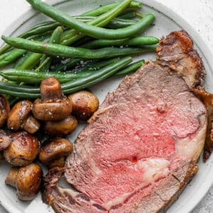 Plate of a slice of prime rib with cooked mushrooms and green beans.