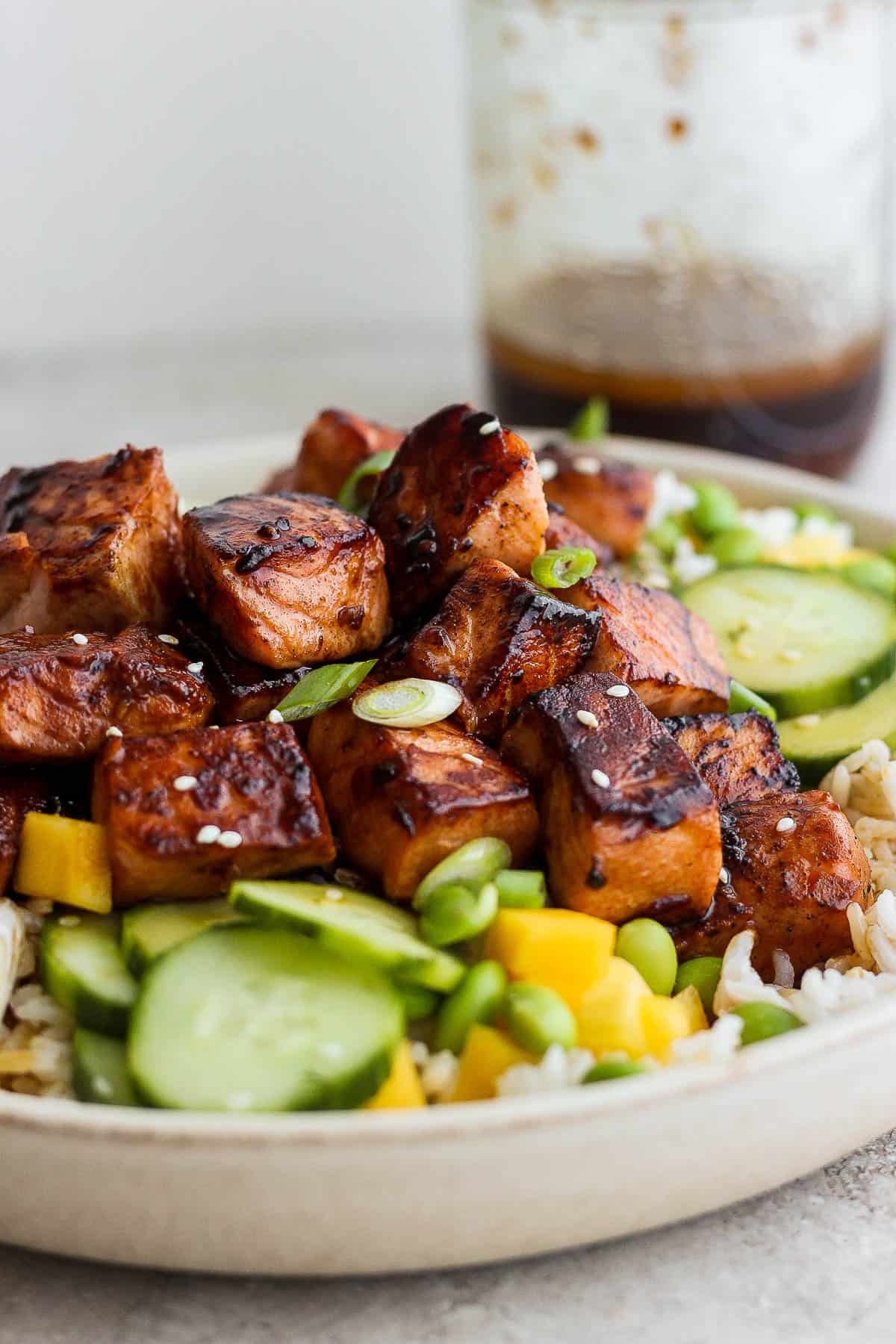 Another image of the marinated and cooked salmon on top of a rice bowl containing rice, mango, edamame, marinated cucumbers, and green onions.