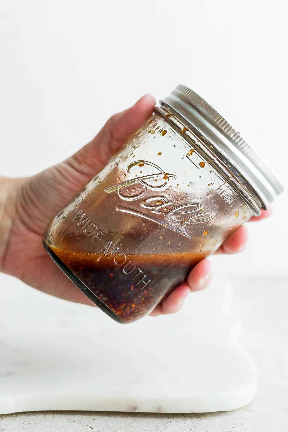 A hand holding a wide mouth Ball jar that contains the salmon marinade inside.