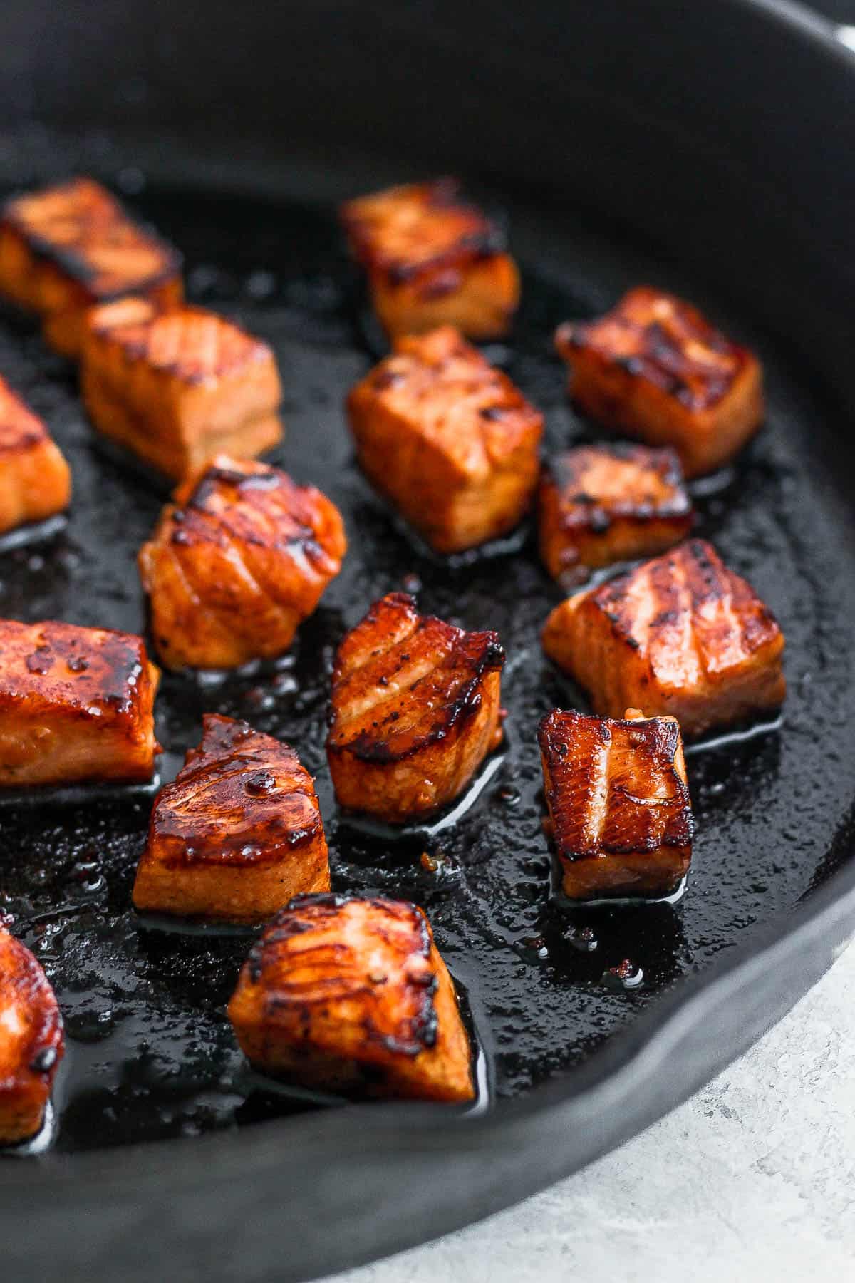 A close up shot of salmon even placed on a cast iron skillet with crispy edges.