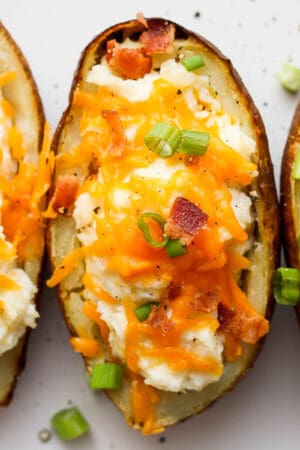 Three twice baked potatoes on a plate topped with cheese, bacon and green onions.