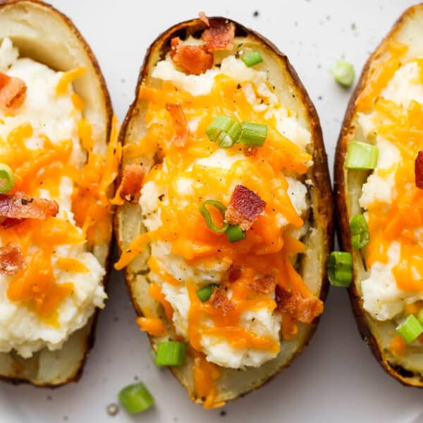 Three twice baked potatoes on a plate topped with cheese, bacon and green onions.