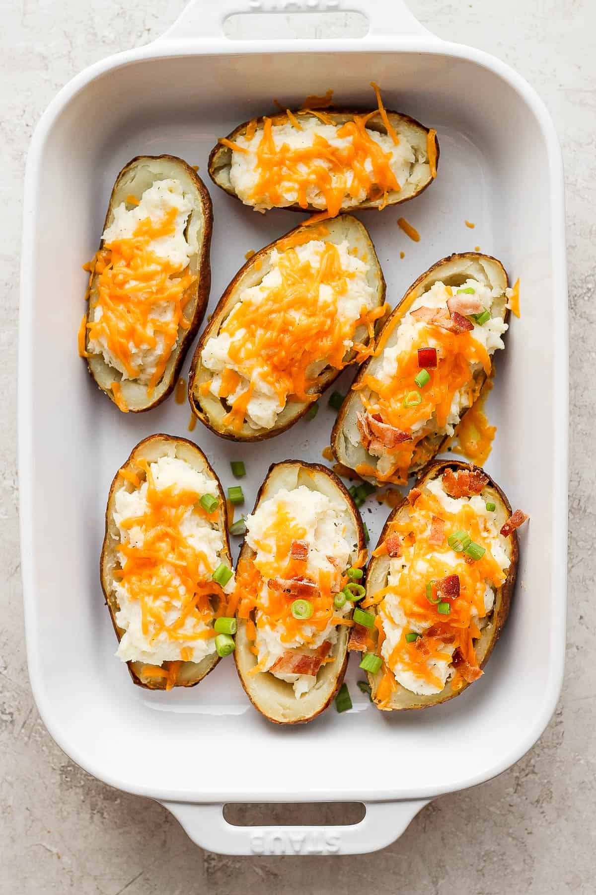 Twice baked potatoes in a large baking dish with some toppings added.