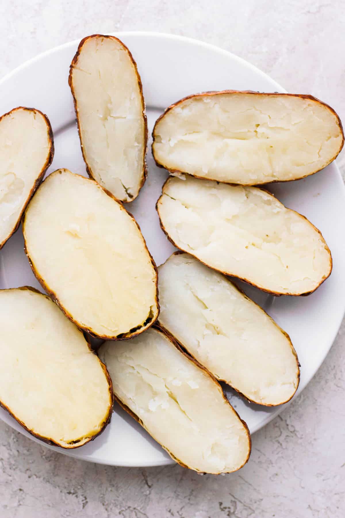 Baked potatoes after being cut in half, lengthwise on a white plate.