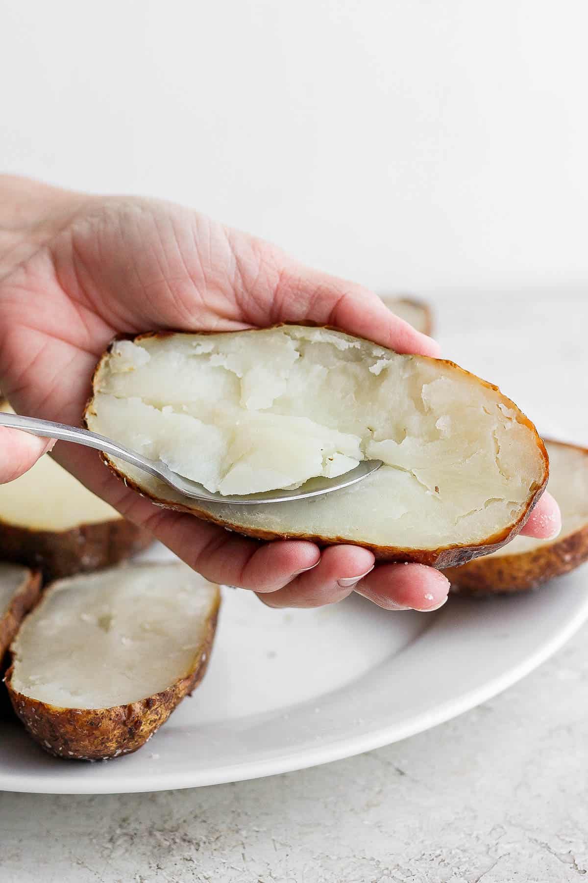 A spoon scooping out the inside of a baked potato half.