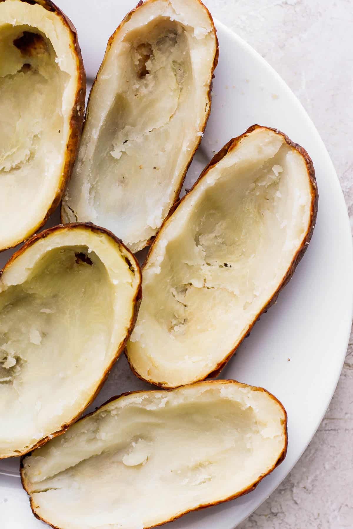 Halves of potatoes on a plate after the inside has been scooped out.