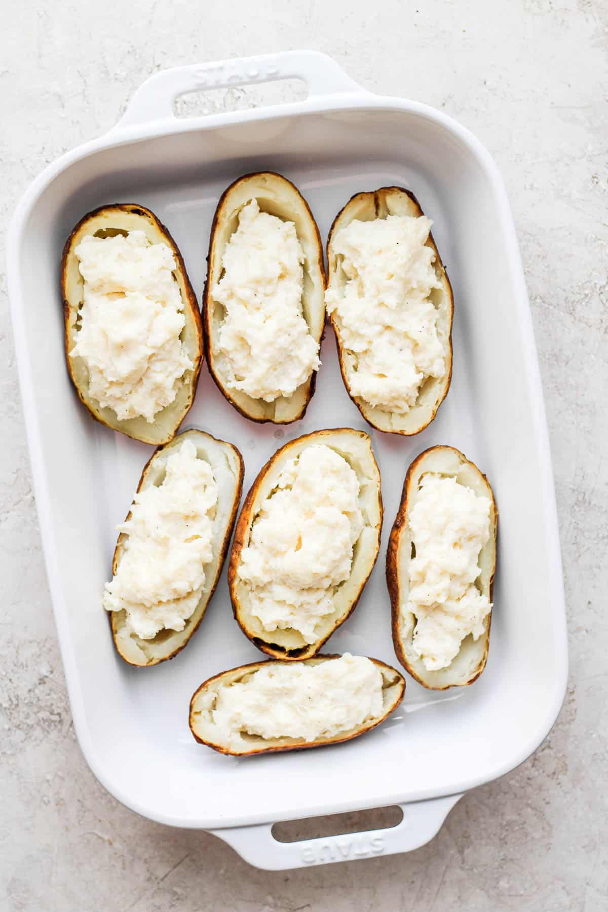 The potato filling added back to the empty potato halves in a large baking dish.