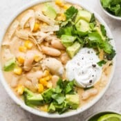 A bowl of white chicken chili topped with cilantro, avocado and cilantro.