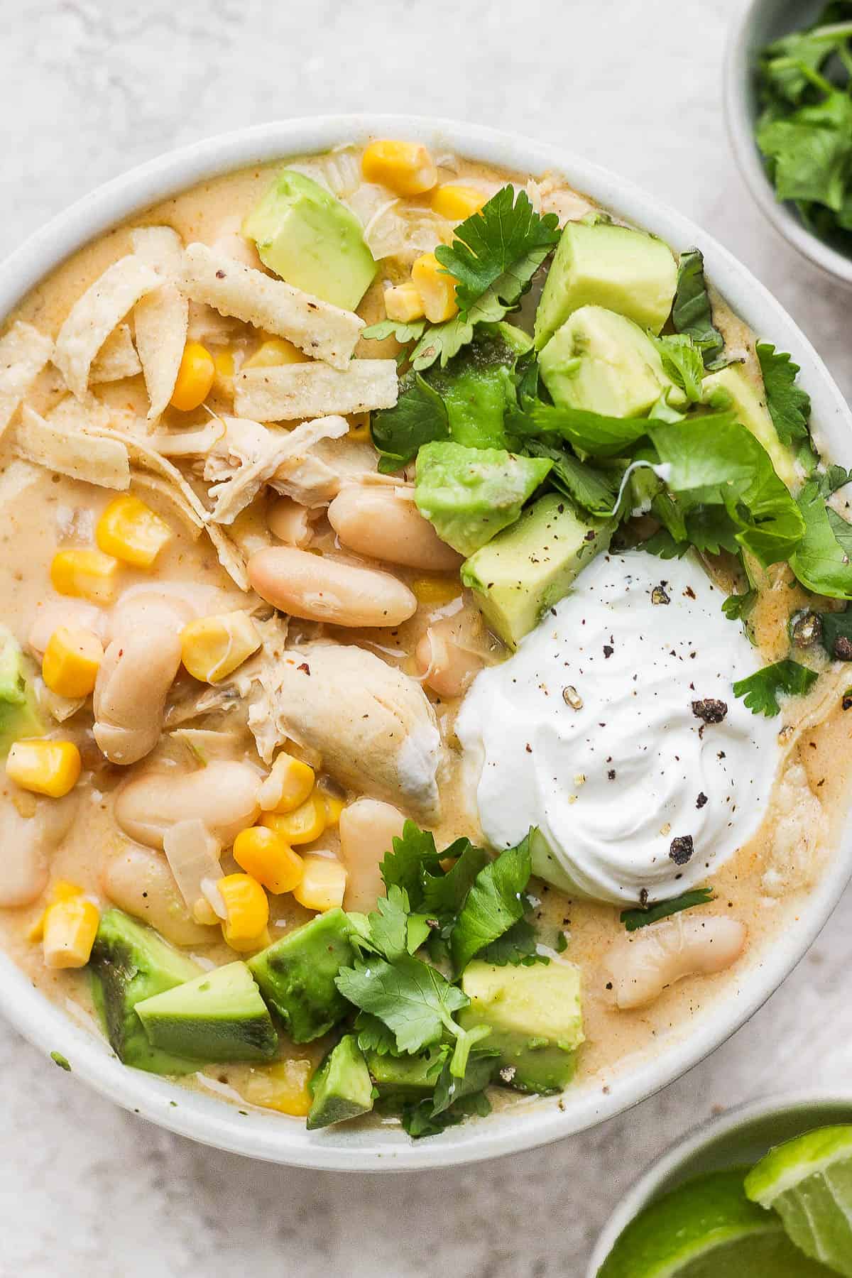 White chicken chili in a white bowl with all the fresh toppings.