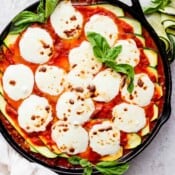 A cast iron skillet filled with zucchini lasagna and topped with fresh, melted mozzarella and fresh basil.