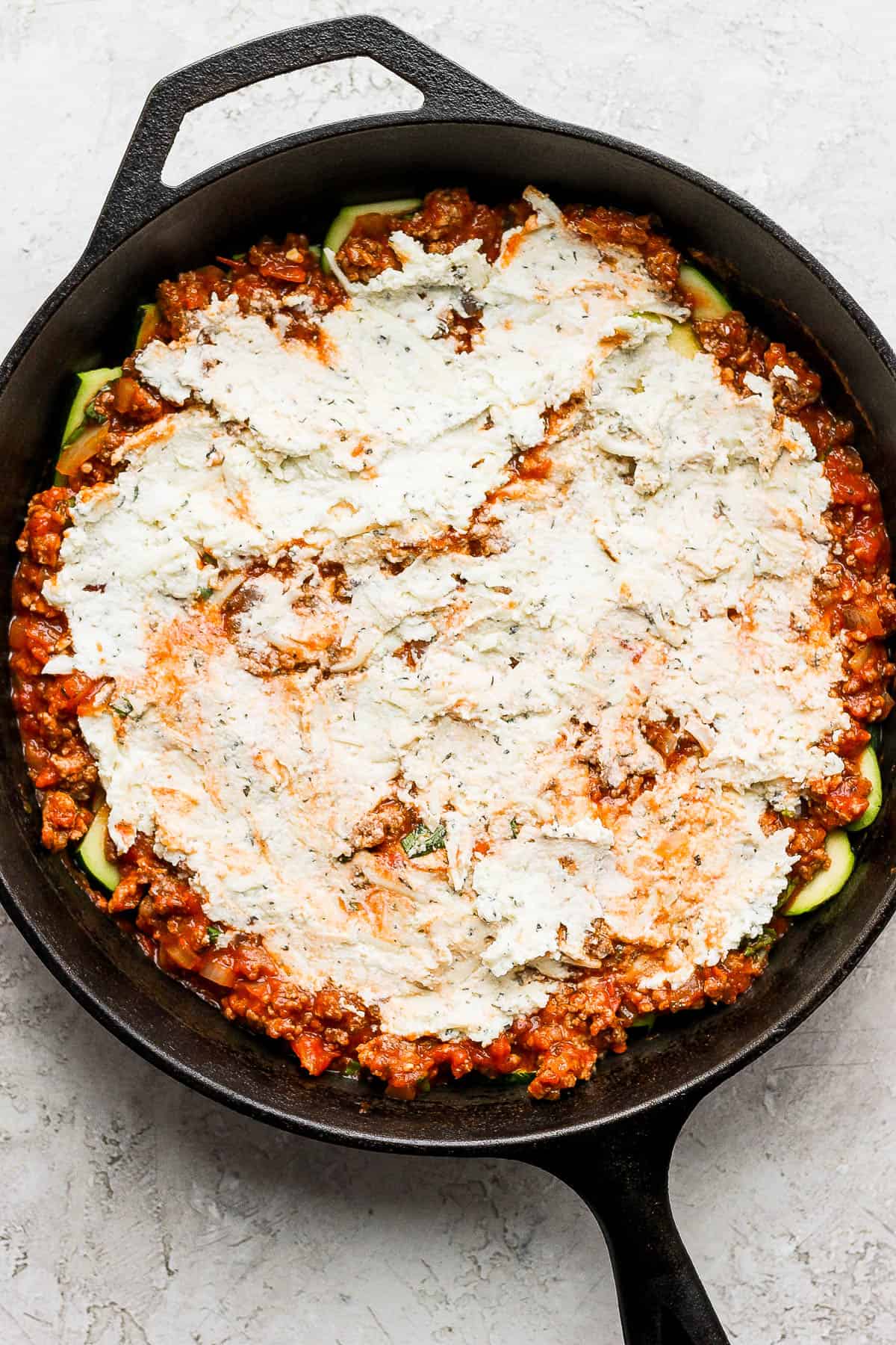 The ricotta cheese mixture spread evenly on top of the meat sauce in the cast iron skillet. 