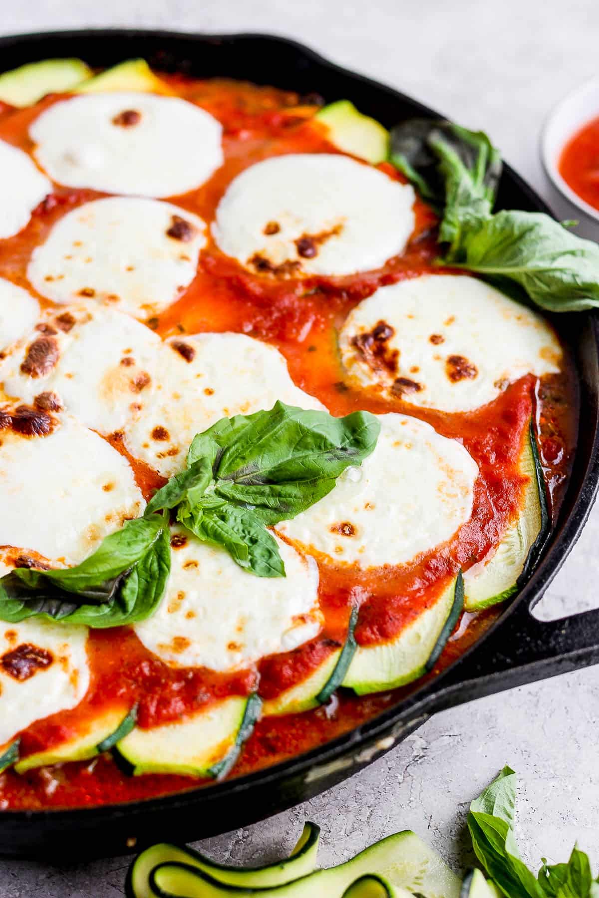 A close up image of the zucchini lasagna showing the melted mozzarella, meat sauce, and layer of zucchinis in the cast iron skillet. 