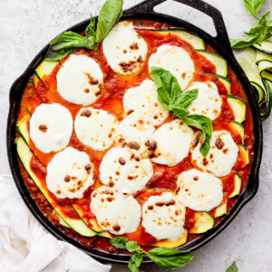 A cast iron skillet filled with zucchini lasagna and topped with fresh, melted mozzarella and fresh basil.