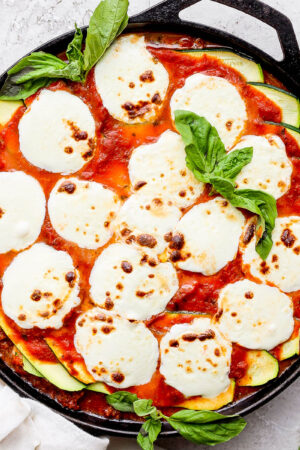 A cast iron skillet filled with zucchini lasagna and topped with fresh, melted mozzarella and fresh basil.