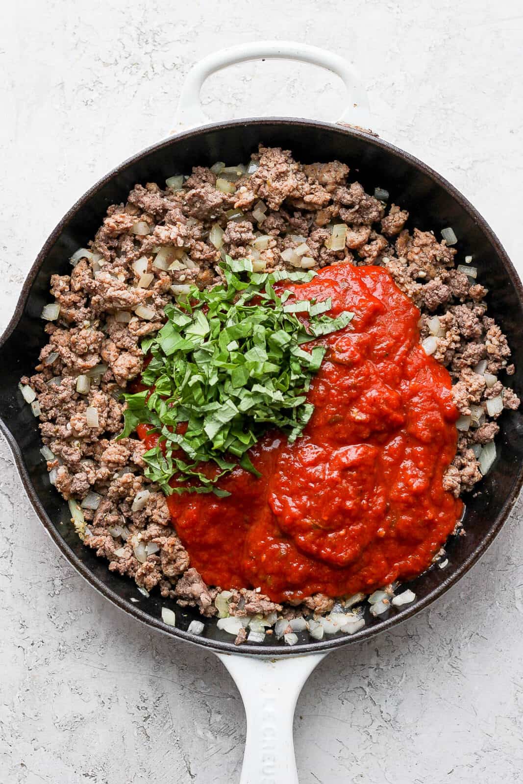 Cooked ground beef, basil, and marinara in a cast iron skillet to make zucchini lasagna with meat sauce.