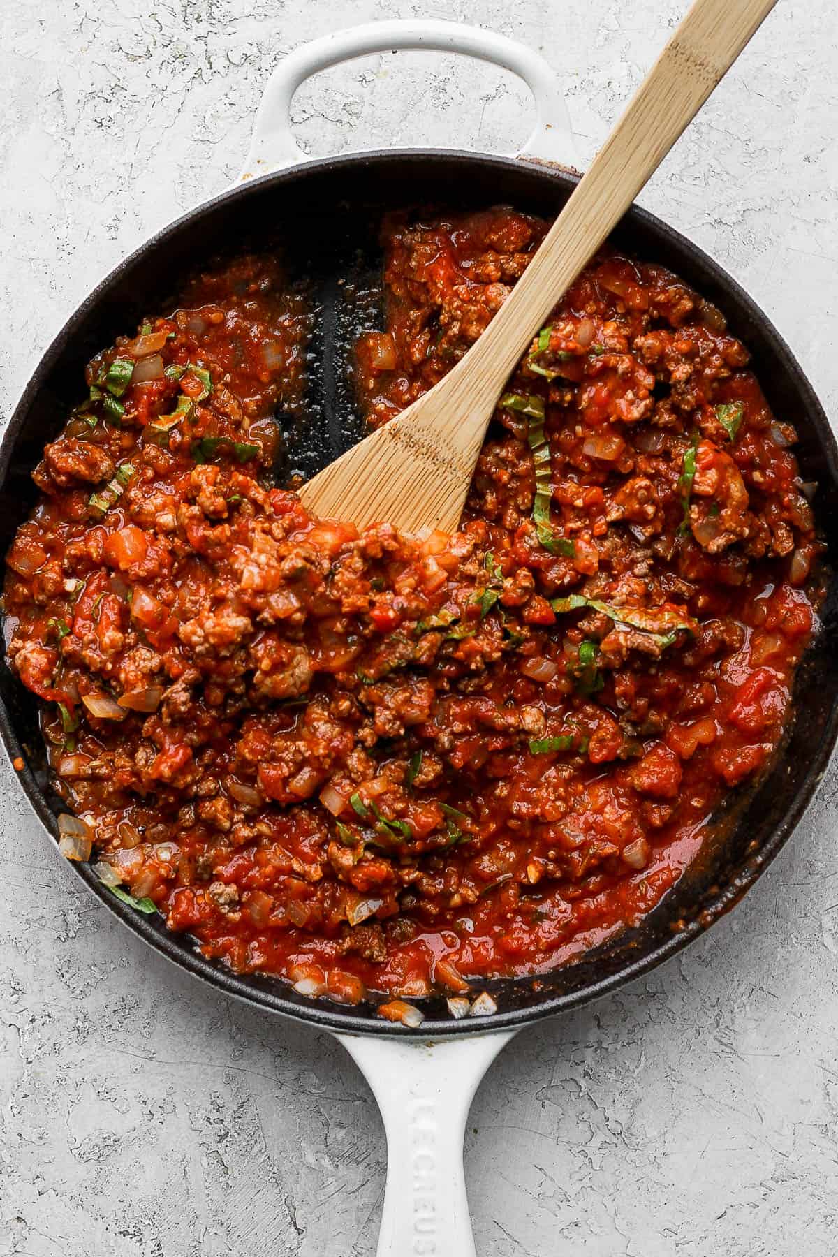 All of the meat sauce ingredients mixed together in a cast iron skillet with a wooden spoon. 