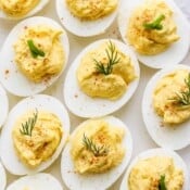 A plate of deviled eggs garnished with fresh dill, chives and paprika.