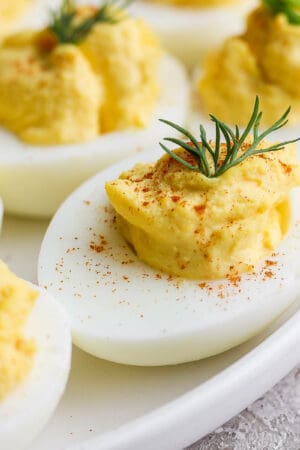 A plate of deviled eggs garnished with fresh dill, chives and paprika.