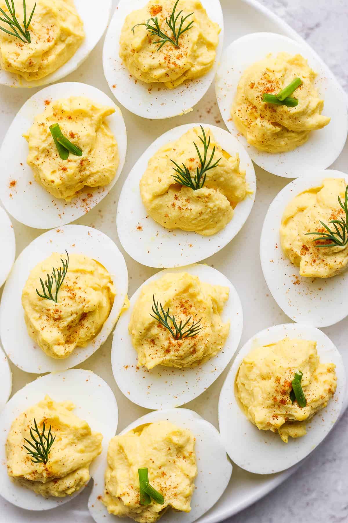 Deviled eggs on a plate topped with paprika, dill and chives.