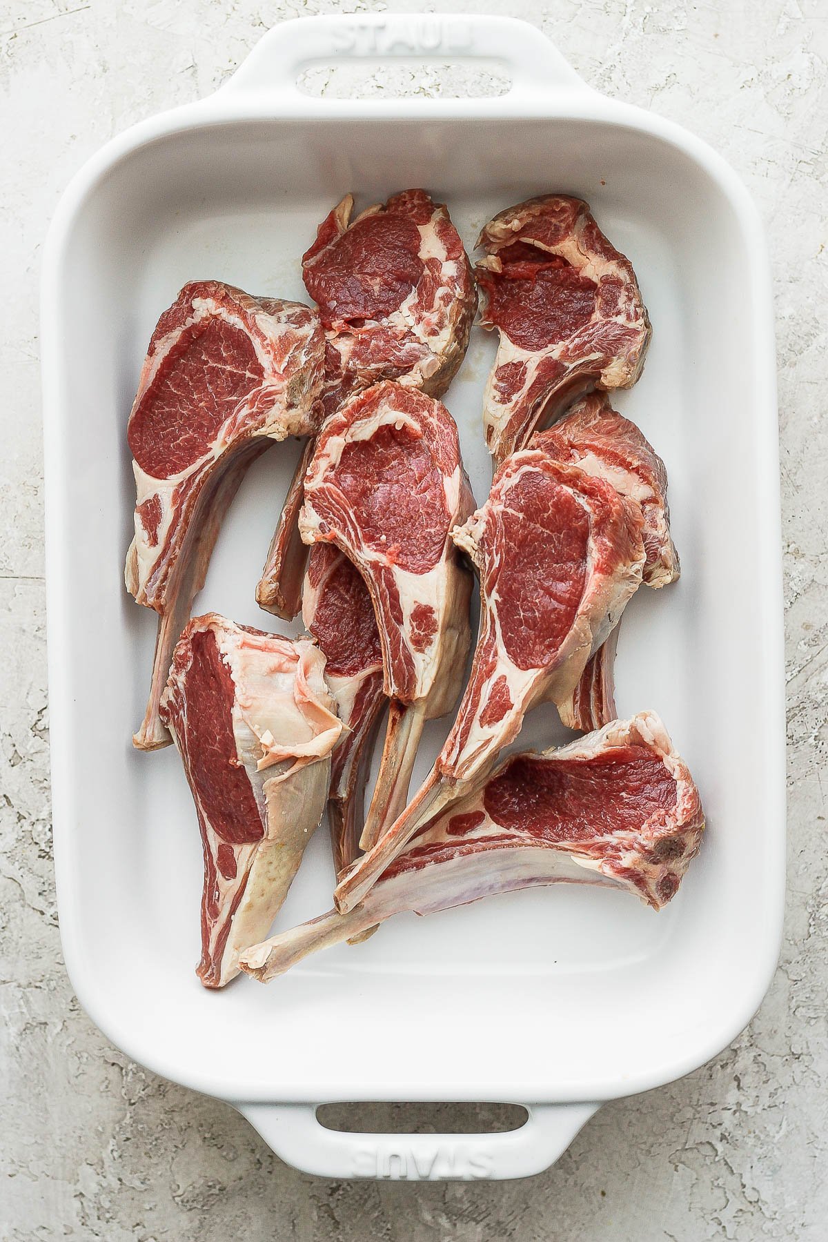 Raw lamb chops in a white baking dish.