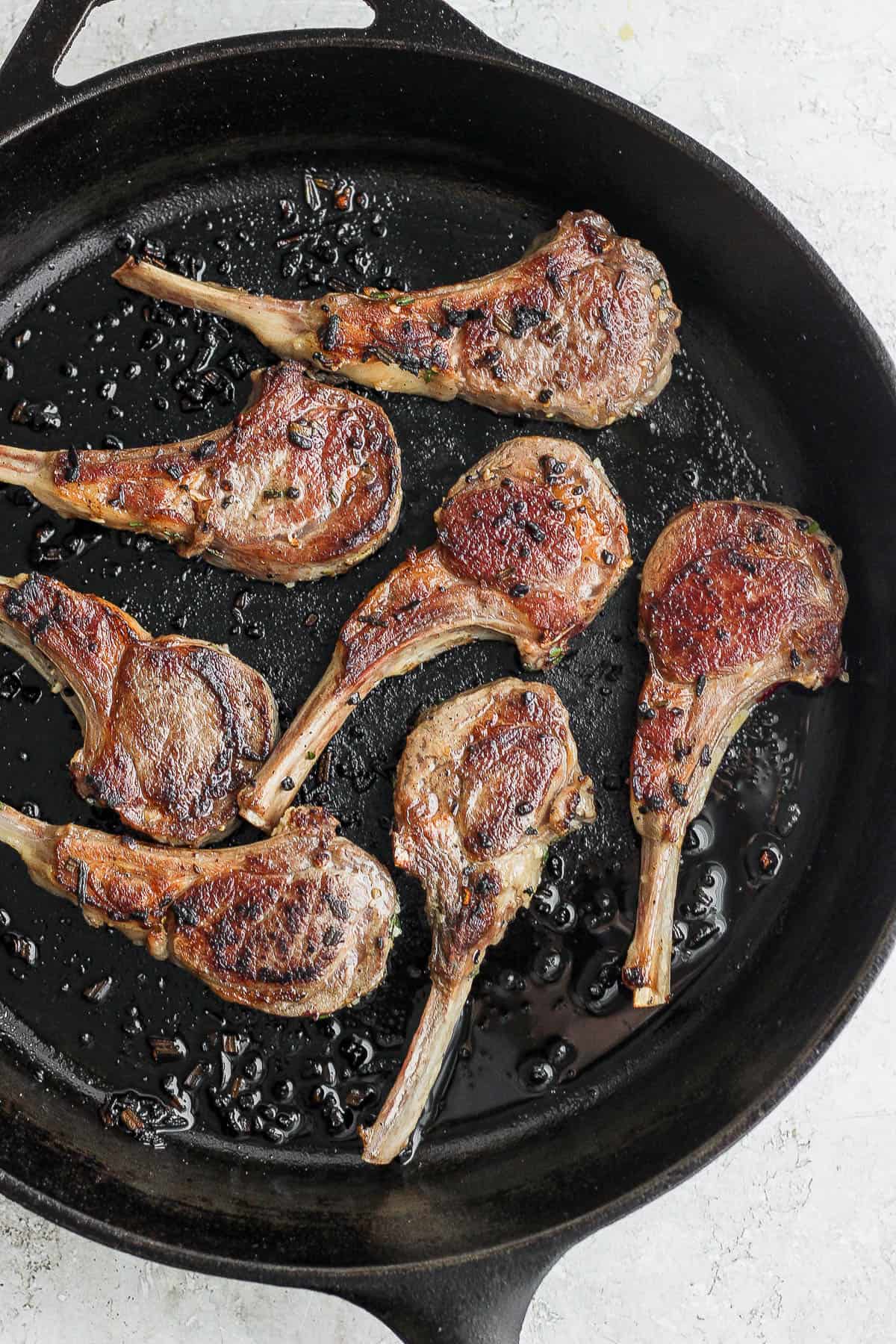 Lamb chops searing in a cast iron skillet.