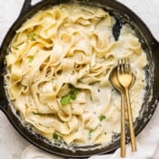A cast iron skillet with noodles and homemade alfredo sauce and a spoon and fork sticking out.