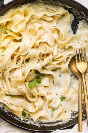 A cast iron skillet with noodles and homemade alfredo sauce and a spoon and fork sticking out.