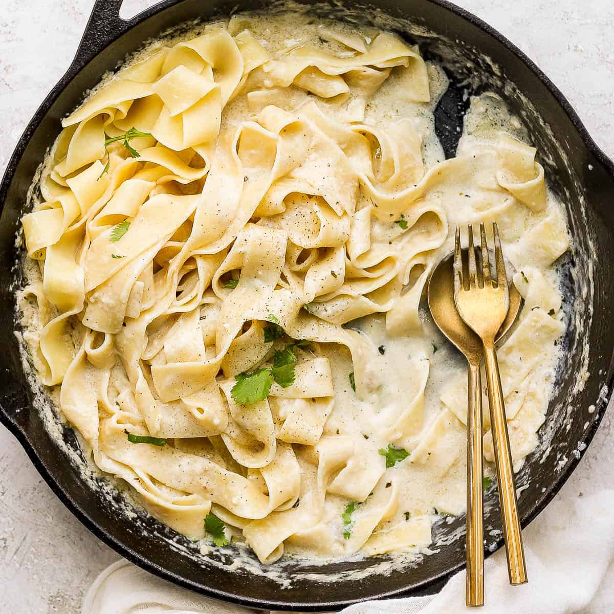 A cast iron skillet with noodles and homemade alfredo sauce and a spoon and fork sticking out.