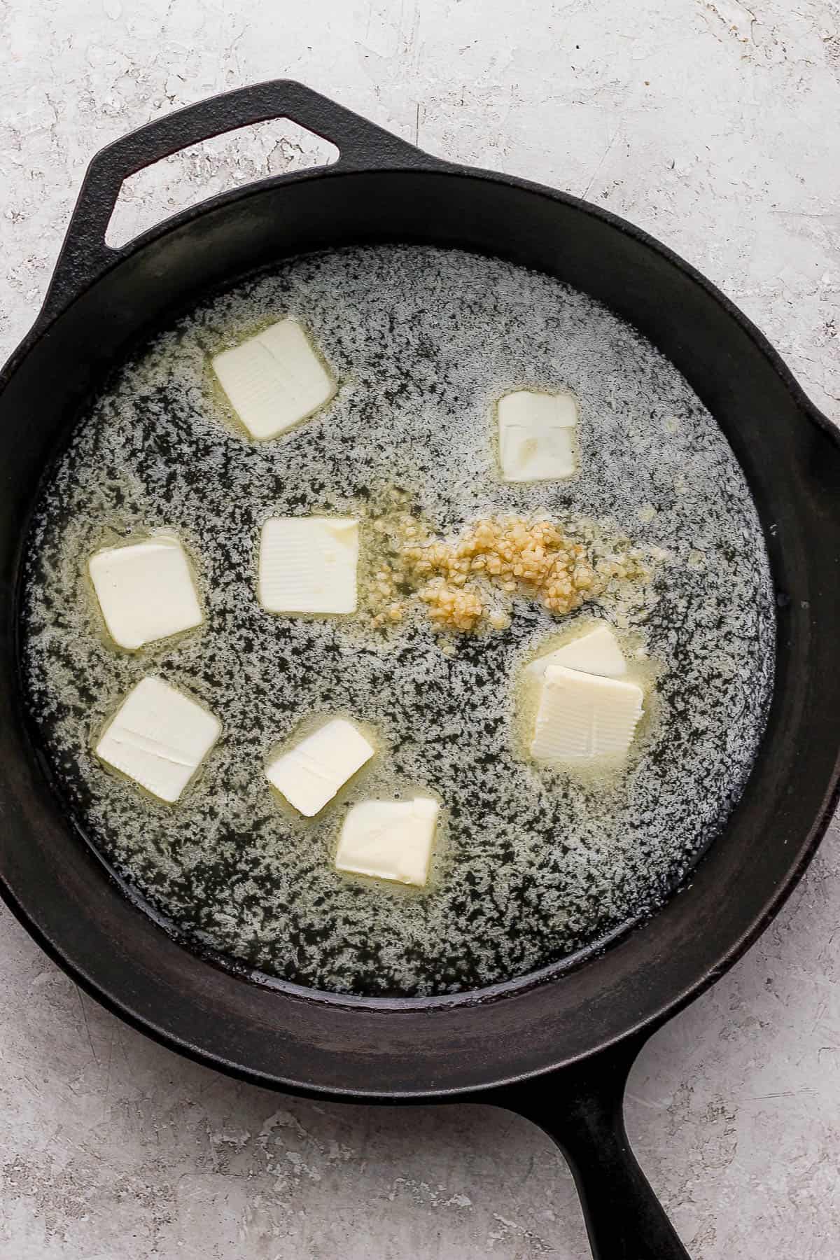 Butter melting in a cast iron skillet with minced garlic added to the pan.