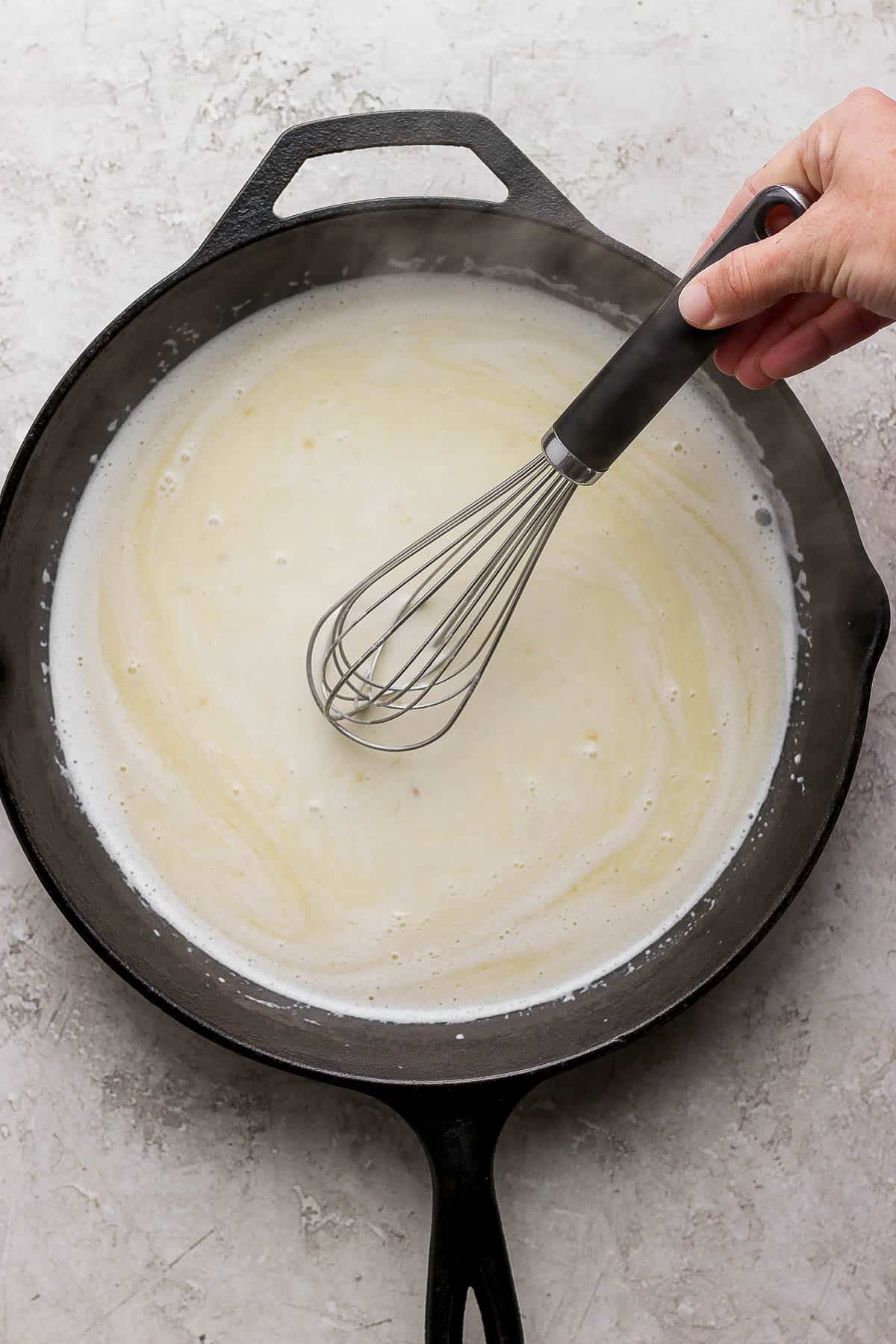A whisk mixing the cream and seasonings into the butter and garlic.