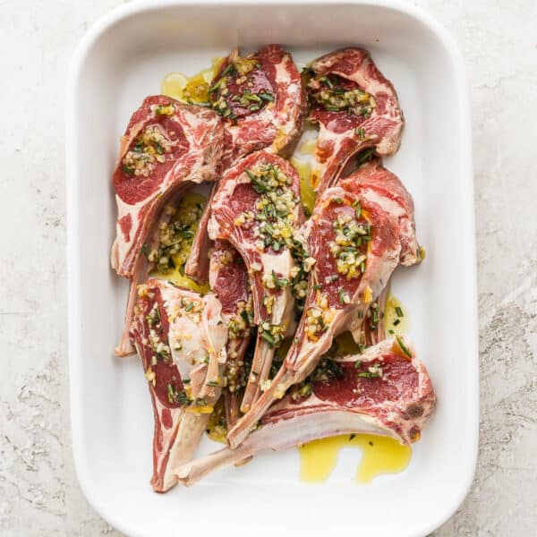 A baking dish filled with lamb chops in a marinaede.