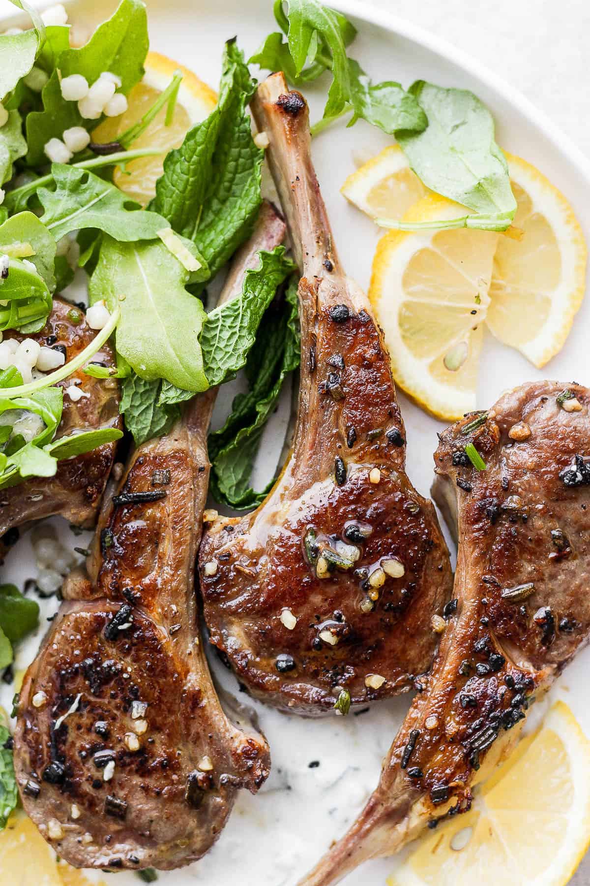 Marinated lamb chops on a plate with a salad and lemon wedges after being cooked.